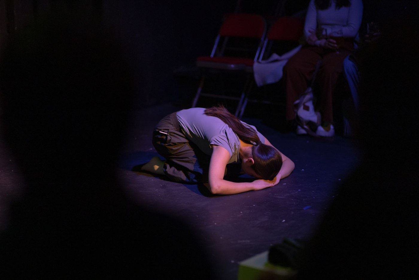 A performer bows low to the floor before a watching audience.