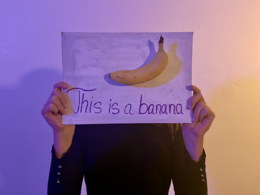 A performer holds up a sign reading "This is a banana" with a banana on it.