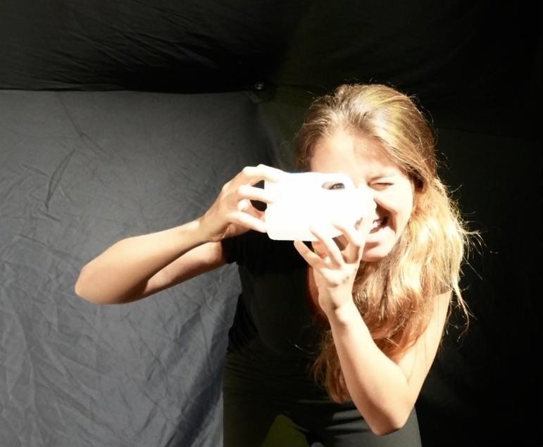 A performer laughs mid-scene, holding an object up to her face.
