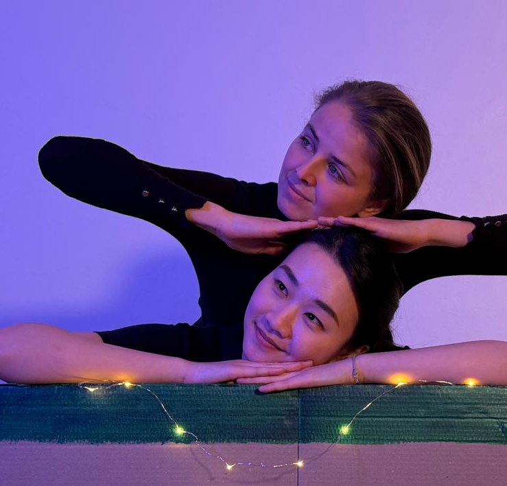 The two performers of Out of the Bin above a fairy-lit cardboard box.