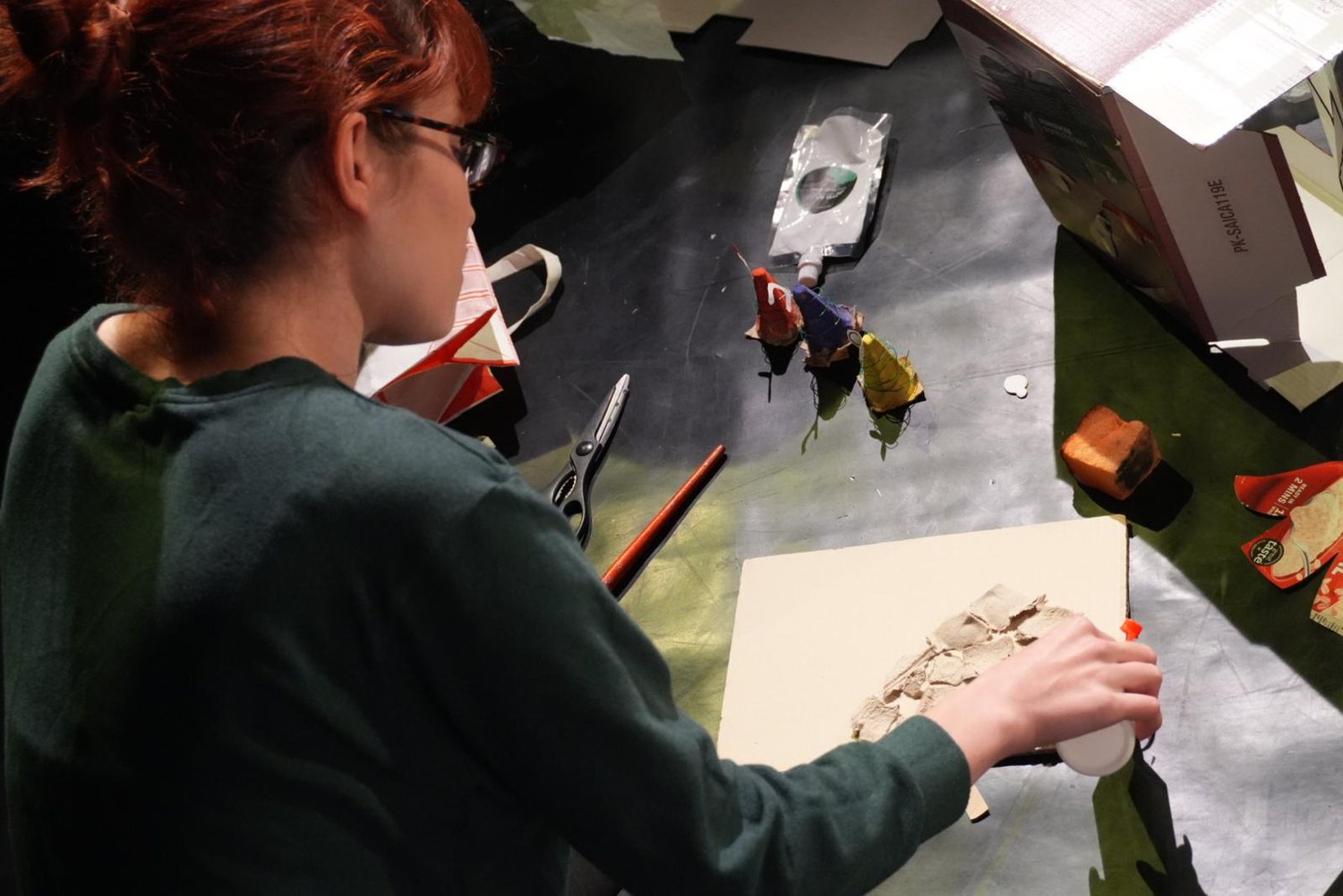 A participant glues pieces of egg carton onto a board during the post-show workshop.