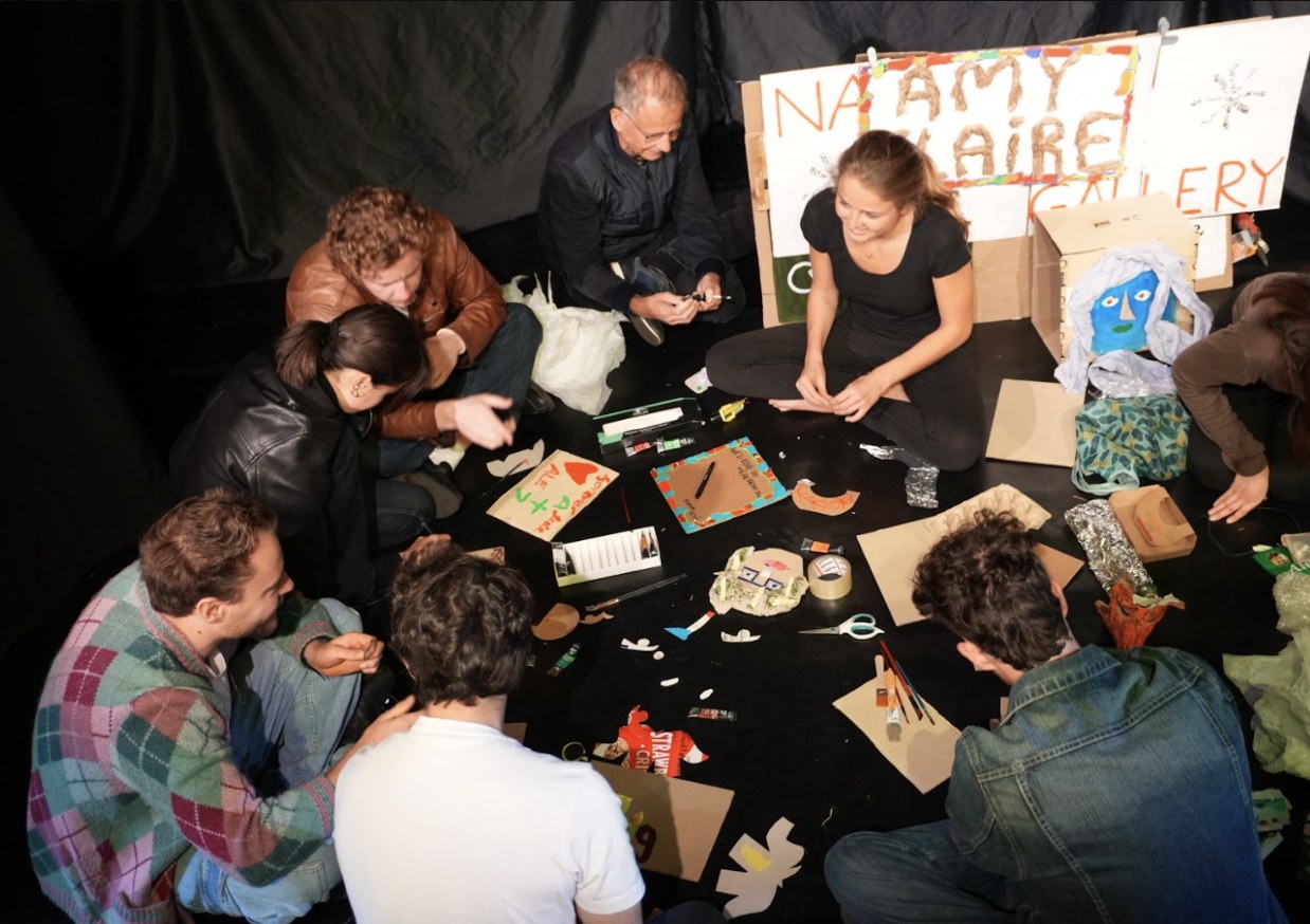 Participants sit in a circle on the floor, making objects from discarded materials.