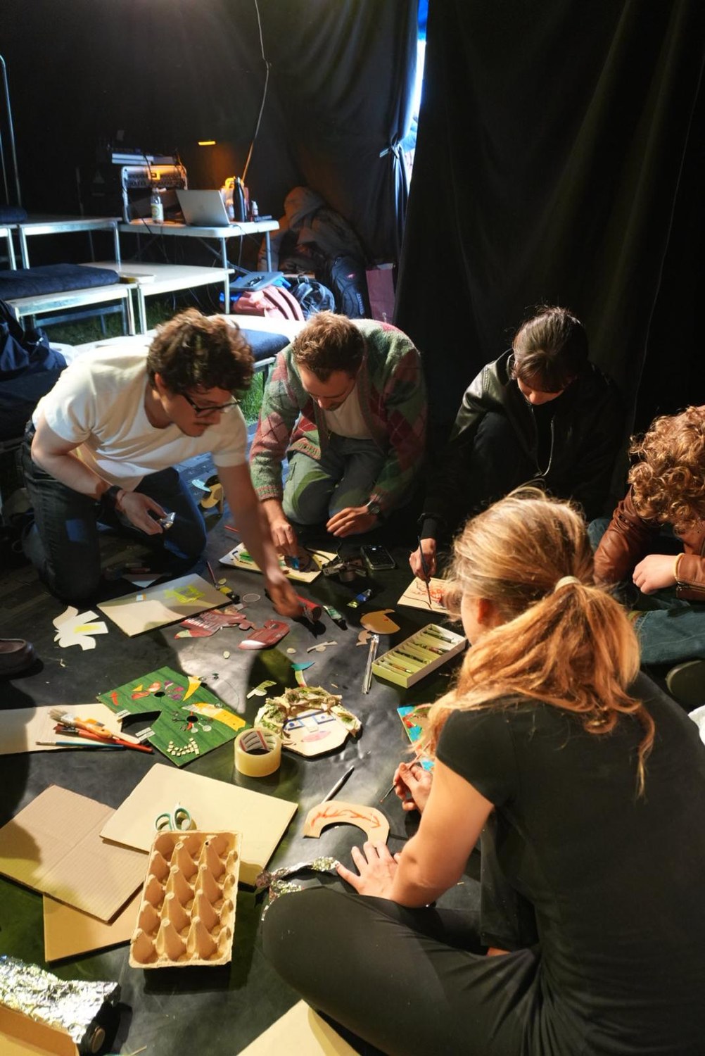 A group of participants kneel on the floor, painting and cutting salvaged materials.