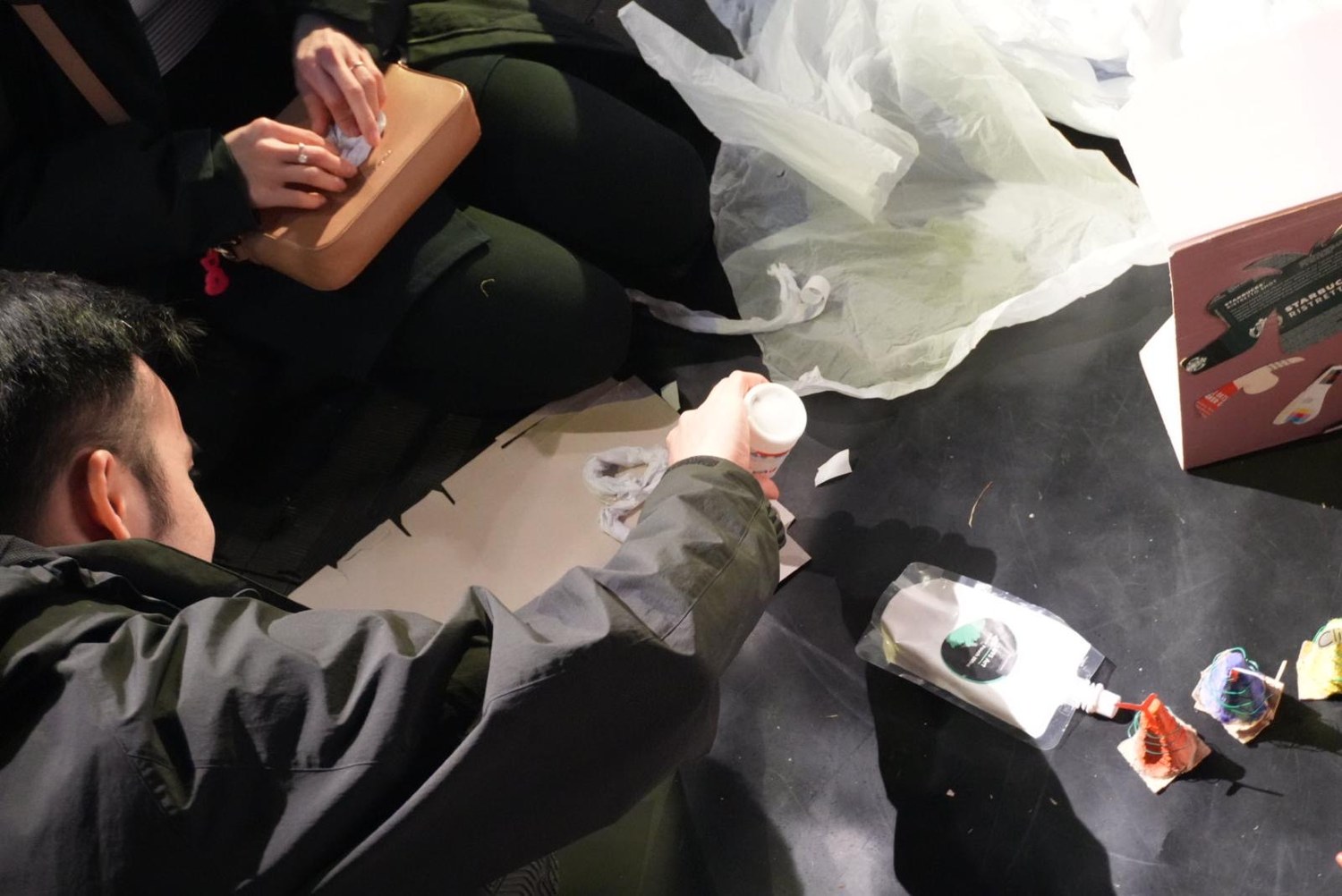 Hands at work with glue, cardboard and a plastic bag during a session.